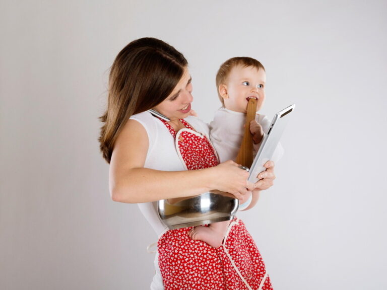 Charge mentale : maman débordée au téléphone qui fait à manger, regarde sa tablette et tient son bébé dans les bras