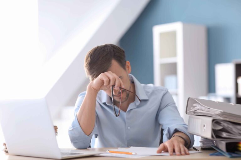 Stress financier : homme decourage et stressé devant son ordinateur et la pile de documents qui l'entourent